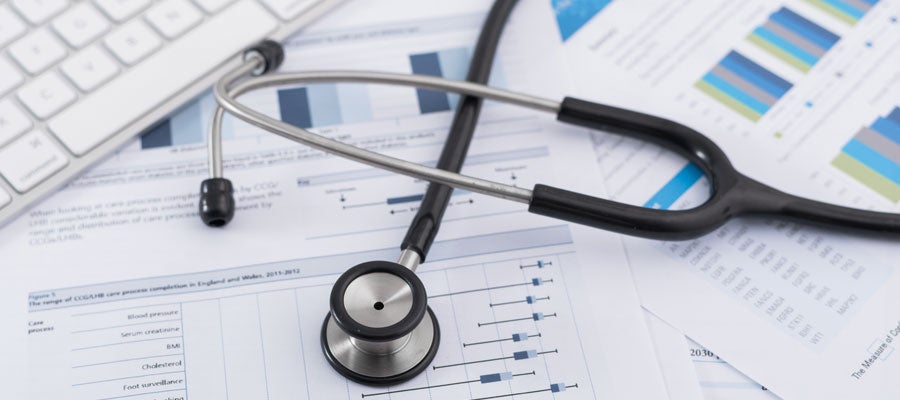 A stethoscope and a keyboard sit sit on data tables and charts