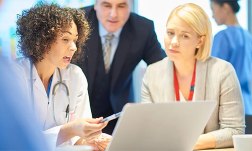 A team of health care executives and professionals huddle around a laptop