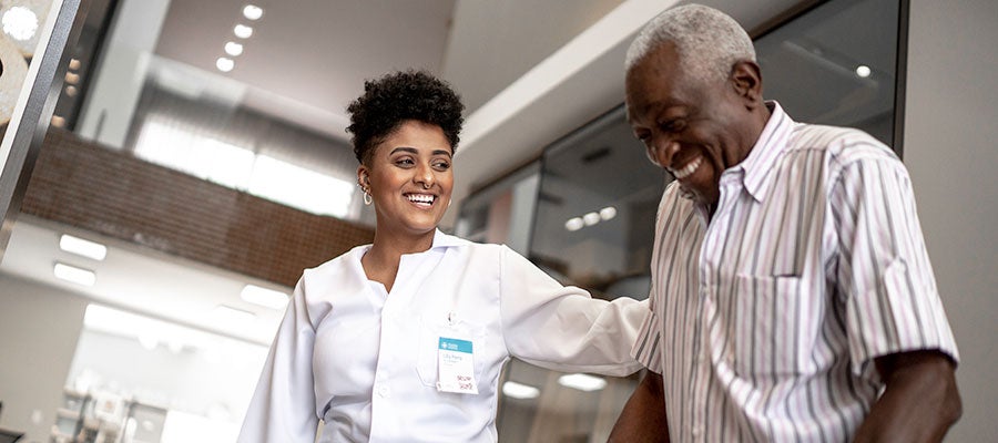 health care worker helping a man using a walker smiling