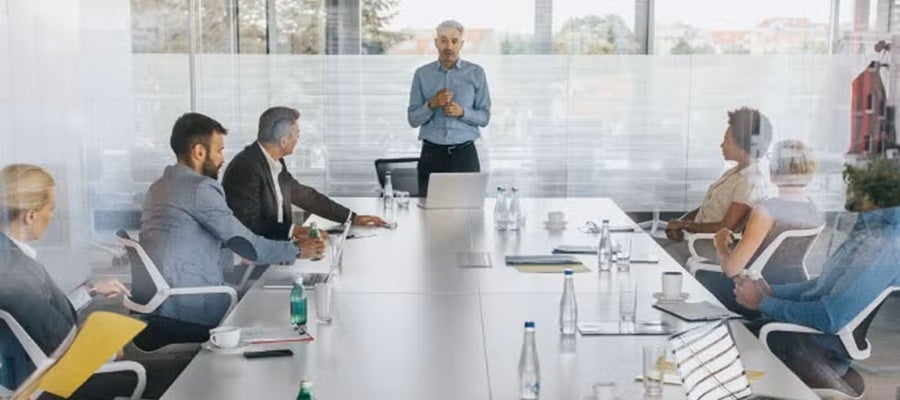 Boardroom 101: Key Strategies and Practical Tools for Orienting New Board Members. A board leader speaking to a board around a large table.