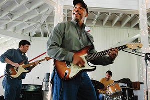 Eugene Woods playing a guitar in front of a rock band.